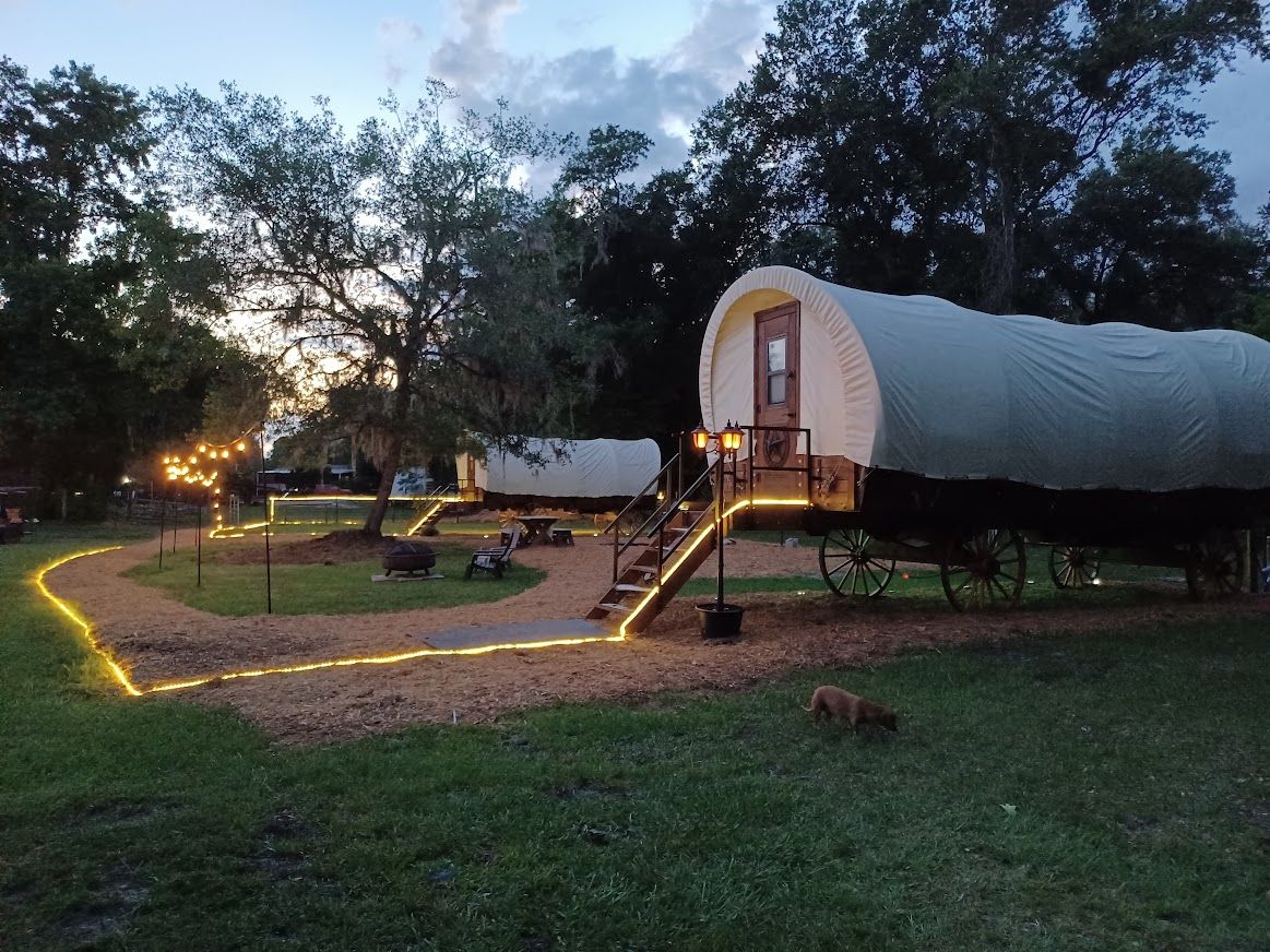 A covered wagon with lit steps and a path of lights at dusk
